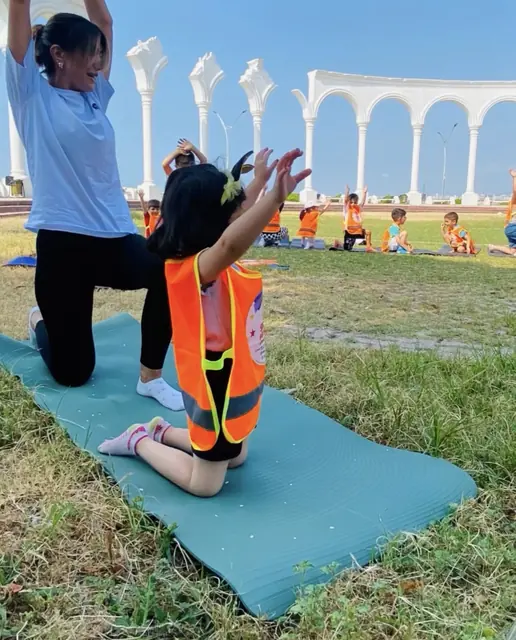 Çim alanda eğitmenle birlikte esneme hareketi yapan çocuk